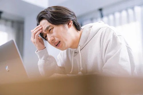 ノートパソコンの前で頭を抱えて悩んでいる男性