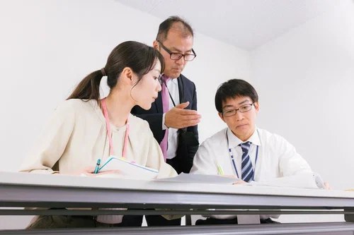 机を囲んで資料を確認しながら打ち合わせをしている3人